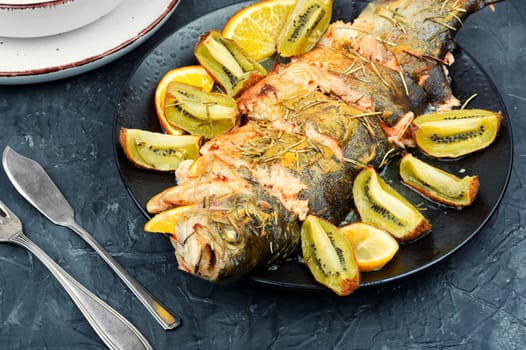 Plate of whole baked trout, served with kiwi fruit and orange.