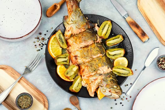 Plate of whole baked trout, served with kiwi fruit and orange.