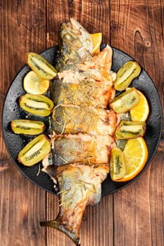Plate of whole baked trout, served with kiwi fruit and orange.