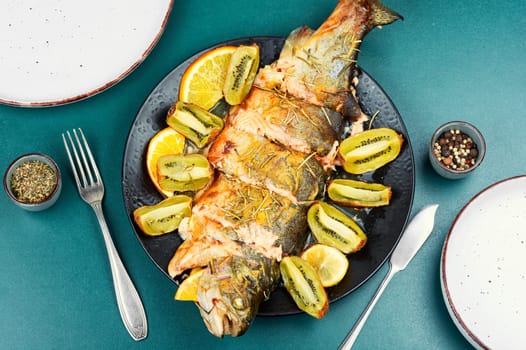 Plate of whole baked trout, served with kiwi fruit and orange.
