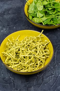 Uncooked spinach pasta tagliatelle with fresh spinach leaves.