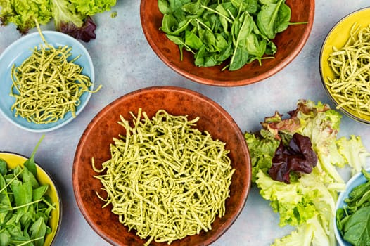 Uncooked spinach pasta tagliatelle with fresh spinach leaves.