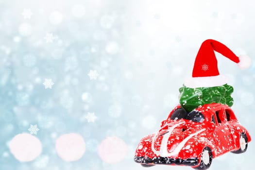 Christmas greeting card template. A snow-covered red car toy with green fir-tree with santa hat on the roof over abstract winter landscape background. Copy space for your design.