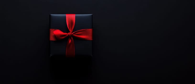 Simple black gift box tied with a striking red ribbon, emphasizing elegance and minimalism on a dark background.