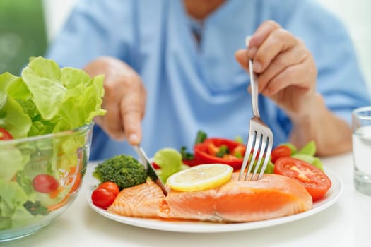Asian elderly woman patient eating salmon stake and vegetable salad for healthy food in hospital.