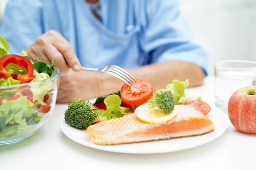 Asian elderly woman patient eating salmon stake and vegetable salad for healthy food in hospital.
