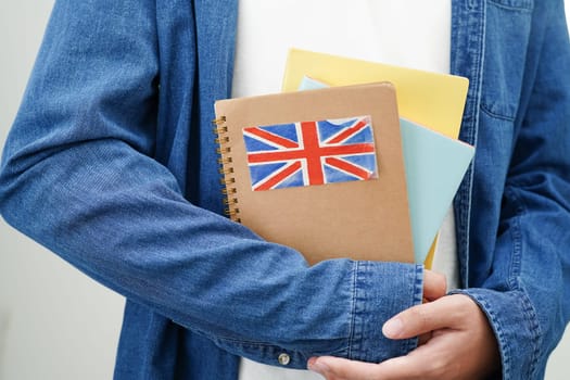 Learning English, Asian teenage student holding book with flag for language program education.