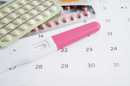 Pregnancy test with birth control pills and condom for female on calendar, ovulation day.