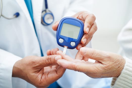 Asian doctor using digital glucose meter for check sample blood sugar level to treatment diabetes.