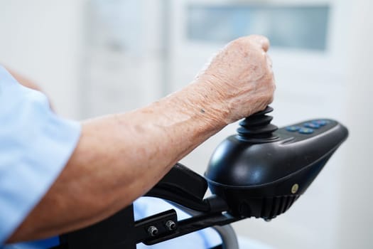 Asian elderly disability woman patient use joystick electric wheelchair in hospital.