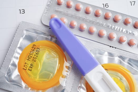 Pregnancy test with birth control pills and condom for female on calendar, ovulation day.