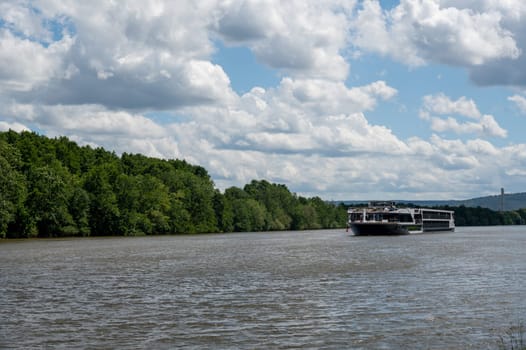 A pleasure boat sails along a river, with green nature, blue sky and white clouds