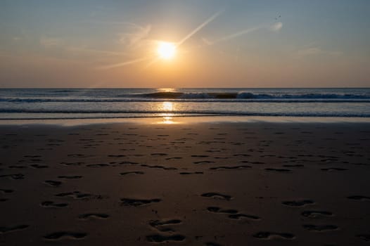 Many footprints in the wet sand by the sea, in the evening light with sea and sunlight