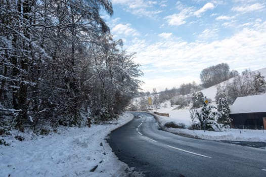 Snow landscape with trees, road and blue sky with clouds