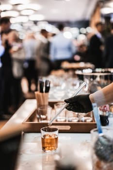 Expert barman is making cocktail at business banquet event in hotel conference center. Blurred businesspeople at banquet event business meeting event in the background.