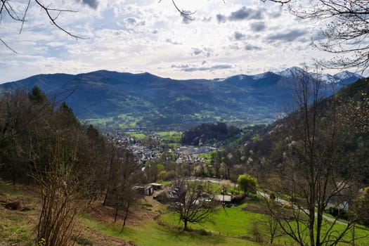 A mountain range with a town in the valley below. The sky is cloudy and the sun is shining through the clouds