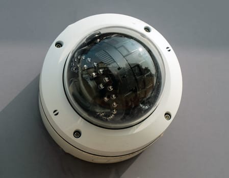 A video camera with a black and white filter is displayed on a grey surface. The lens is round