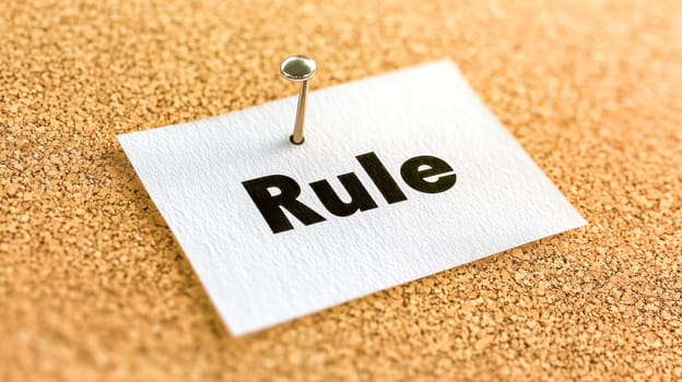 Push pin holds a paper with rule on a cork board, reminding of following office policies. Emphasizing order and structure
