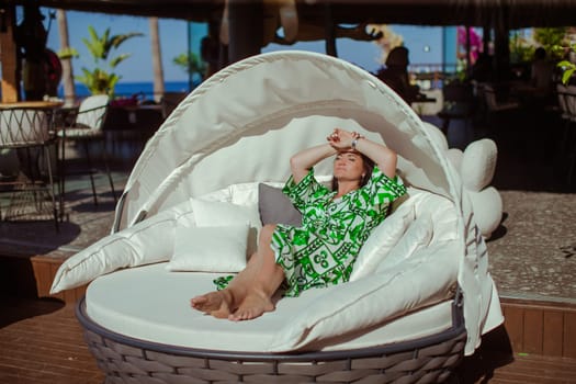 A brunette girl in a green cape is lying on a beach couch