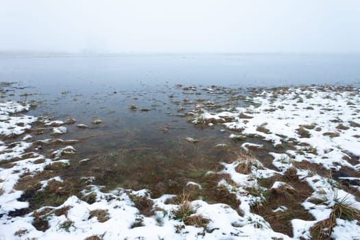 Water and snow on a flooded meadow in the foggy day, Czulczyce, Poland