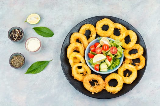 Delicious Fried squid rings and fresh vegetable salad on stone table background. Copy space.