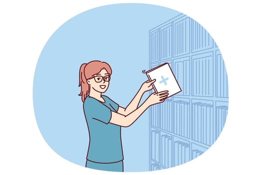 Woman clinic administrator with patient card stands near rack with archive of patients who visited hospital. Girl doctor works in archive of clinic taking care of data and cards with diagnoses