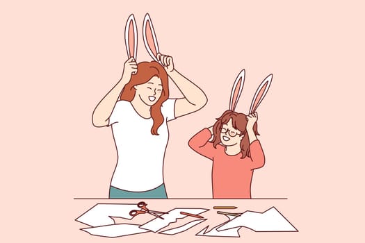 Family creativity for mom and daughter cutting out bunny ears from paper or preparing for christmas masquerade. Older and younger sister are engaged in family creativity, enjoying live communication