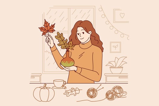 Woman collects bouquet of autumn leaves and places them in vase to decorate home on thanksgiving eve. Girl rejoices at arrival of autumn and makes decorations for apartment, creating cozy atmosphere