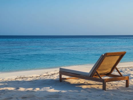 A solitary beach lounger faces the tranquil sea, inviting relaxation on a sandy shore under a clear blue sky.