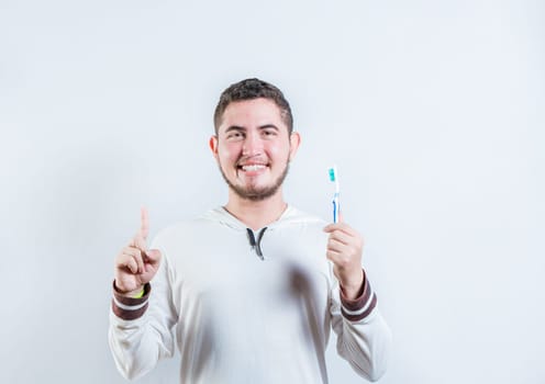 Positive young man holding toothbrush pointing up. Happy guy holding toothbrush and pointing up