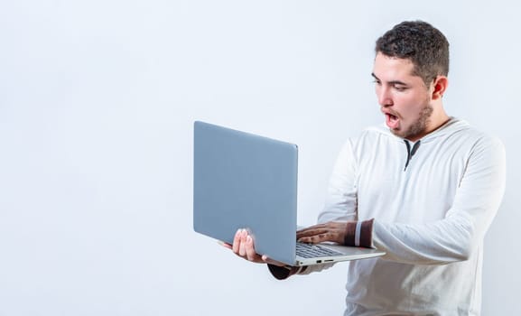 Amazed handsome man standing using laptop isolated. Surprised guy holding and looking at an promotion on laptop screen