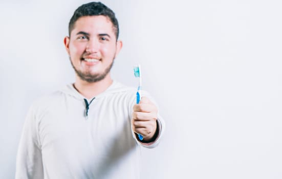 Young man holding toothbrush and looking at camera isolated. Oral health concept