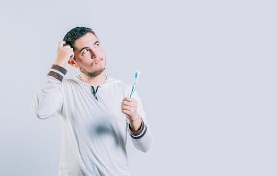 Thoughtful guy holding toothbrush looking up isolated. Worried young man holding toothbrush isolated.