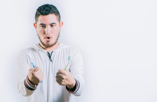 Surprised handsome guy holding toothbrushes isolated. Amazed teen guy holding two toothbrush isolated