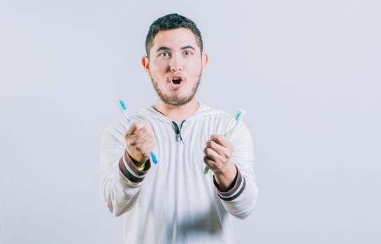 Amazed teen guy holding two toothbrush looking at camera isolated. Surprised people holding toothbrushes isolated
