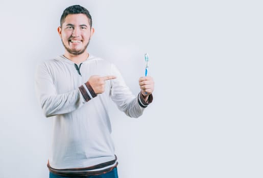 Happy guy pointing at toothbrush isolated. Handsome man holding and pointing toothbrush isolated