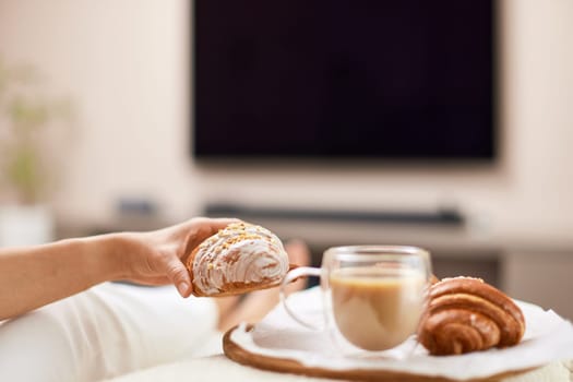 female hand holding fresh french croissants and glass of coffee for breakfast in bed in the morning, tasty breakfast