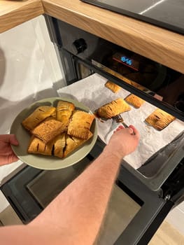 Freshly baked pastries are being taken out of the oven, steaming and golden brown, ready to be served on a green plate. Aroma of crispy dough fills the cozy kitchen, evoking a sense of warmth and homemade goodness.