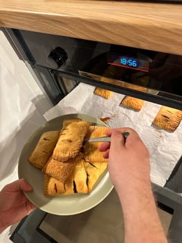 Freshly baked pastries are being taken out of the oven, steaming and golden brown, ready to be served on a green plate. Aroma of crispy dough fills the cozy kitchen, evoking a sense of warmth and homemade goodness.
