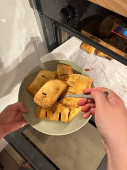 Freshly baked pastries are being taken out of the oven, steaming and golden brown, ready to be served on a green plate. Aroma of crispy dough fills the cozy kitchen, evoking a sense of warmth and homemade goodness.