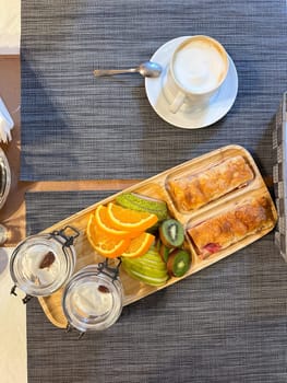colorful breakfast spread showcases sliced fruits and pastries on a wooden tray, offering a vibrant start to the day. accompanied by glasses of water, this arrangement exudes freshness and simplicity