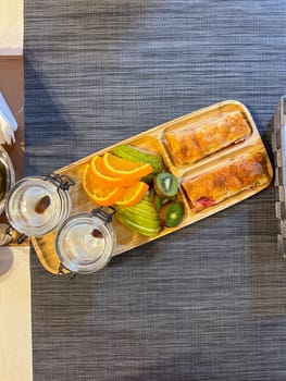 colorful breakfast spread showcases sliced fruits and pastries on a wooden tray, offering a vibrant start to the day. accompanied by glasses of water, this arrangement exudes freshness and simplicity