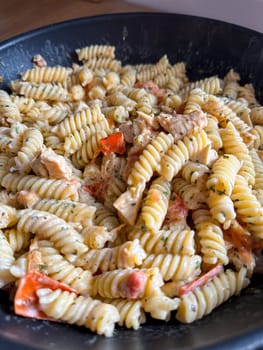 Delicious bowl of creamy rotini pasta mixed with pieces of chicken and vibrant vegetables is served fresh and ready to eat. Dish showcases a perfect blend of flavors and textures, making it an appetizing choice for any meal.