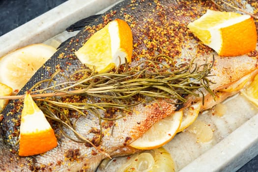 Whole baked trout on a stylish stone plate with orange on wooden background.