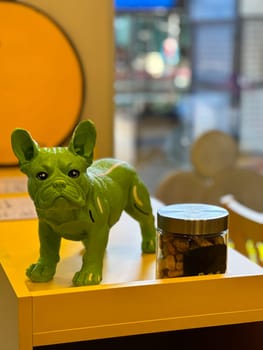 Vibrant green dog statue stands elegantly on a yellow shelf beside a jar of treats. Playful and cheerful atmosphere in room. Treats for pet dogs.
