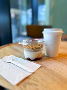 Morning breakfast of yogurt parfait with granola and a hot coffee to go in a cozy cafe setting. Relaxing and inviting atmosphere perfect for breakfast.