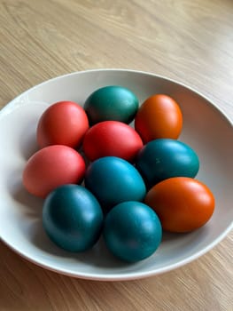 Bowl of vibrant colored Easter eggs standing on a wooden surface, beautifully festive and joyful atmosphere. Easter and religious holidays.