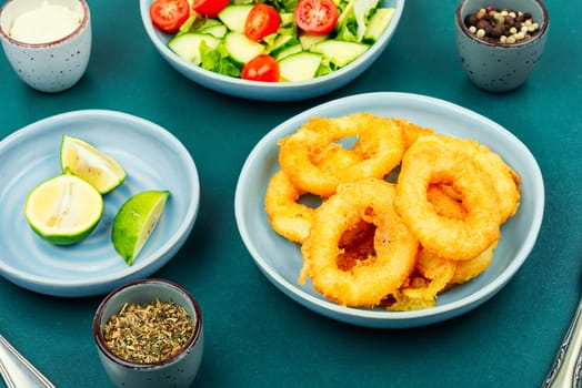 Calamari, fried squid rings with raw vegetable salad on rustic wooden table.