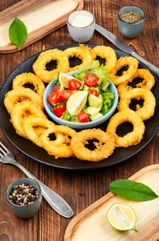 Calamari, fried squid rings with raw vegetable salad on rustic wooden table.