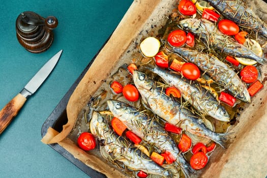 Oven baked Italian fish sardoncini or sardines, with tomatoes, lemon and rosemary on a rustic baking tray.